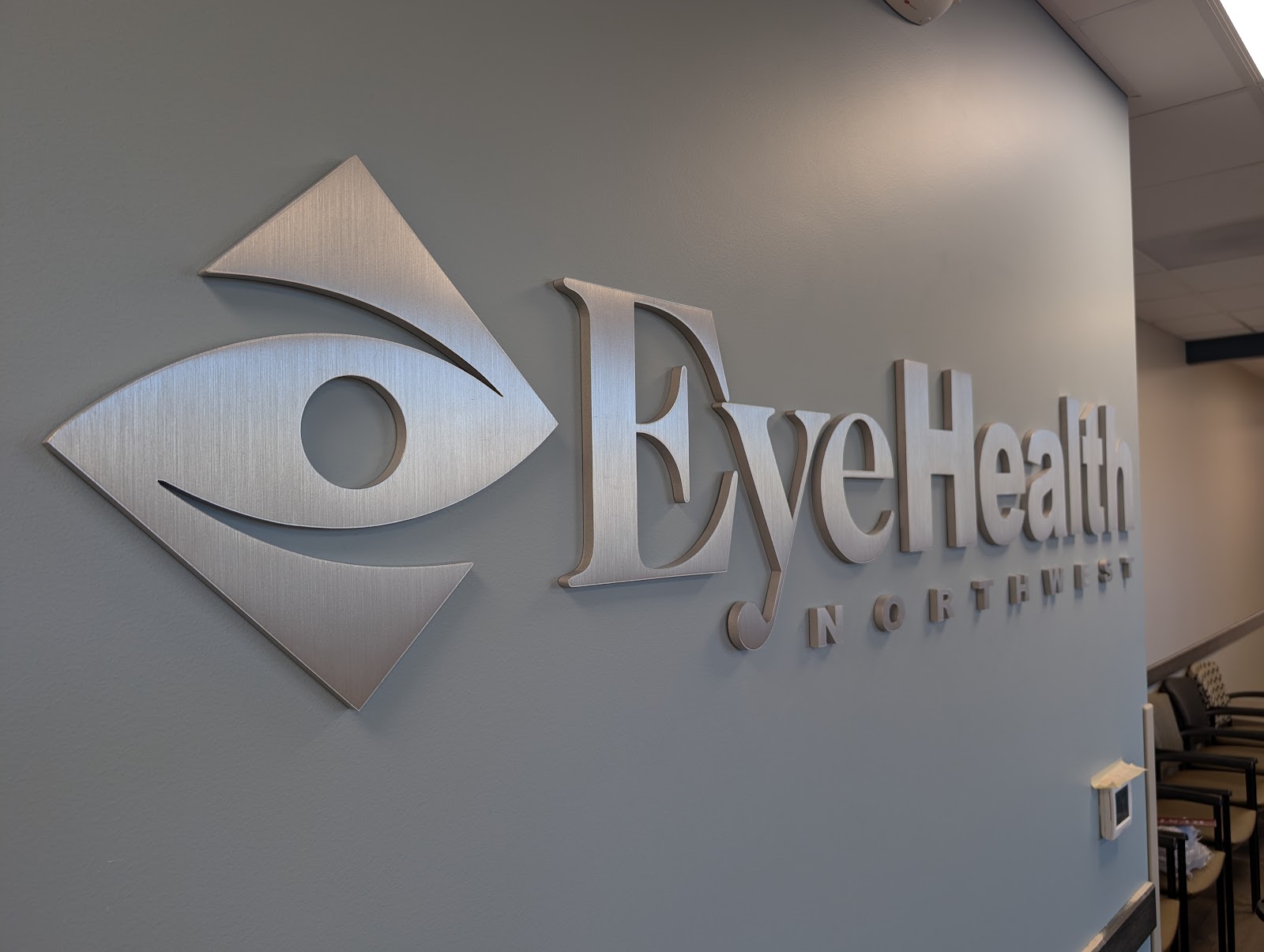 Brushed metal lobby sign with logo and text on a gray wall in Portland, OR.