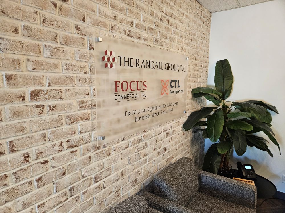 Clear acrylic lobby sign with printed logos and text on a brick wall in Portland, OR.